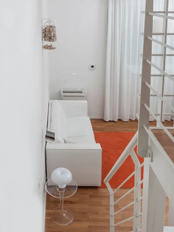 Soggiorno minimalista con divano bianco, tappeto arancione e scala vista dall'alto