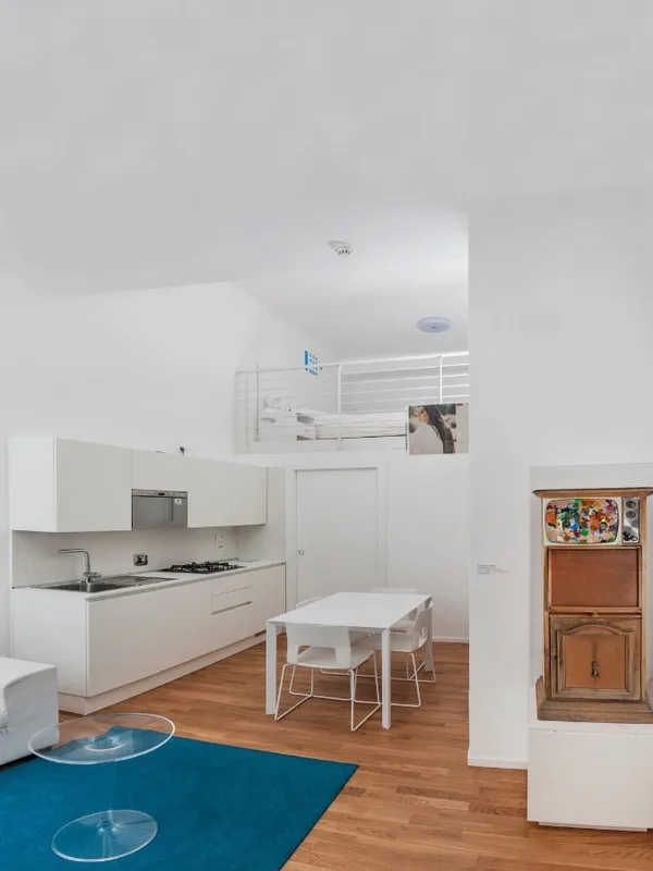 Open space con cucina bianca, zona pranzo e soppalco con letto
