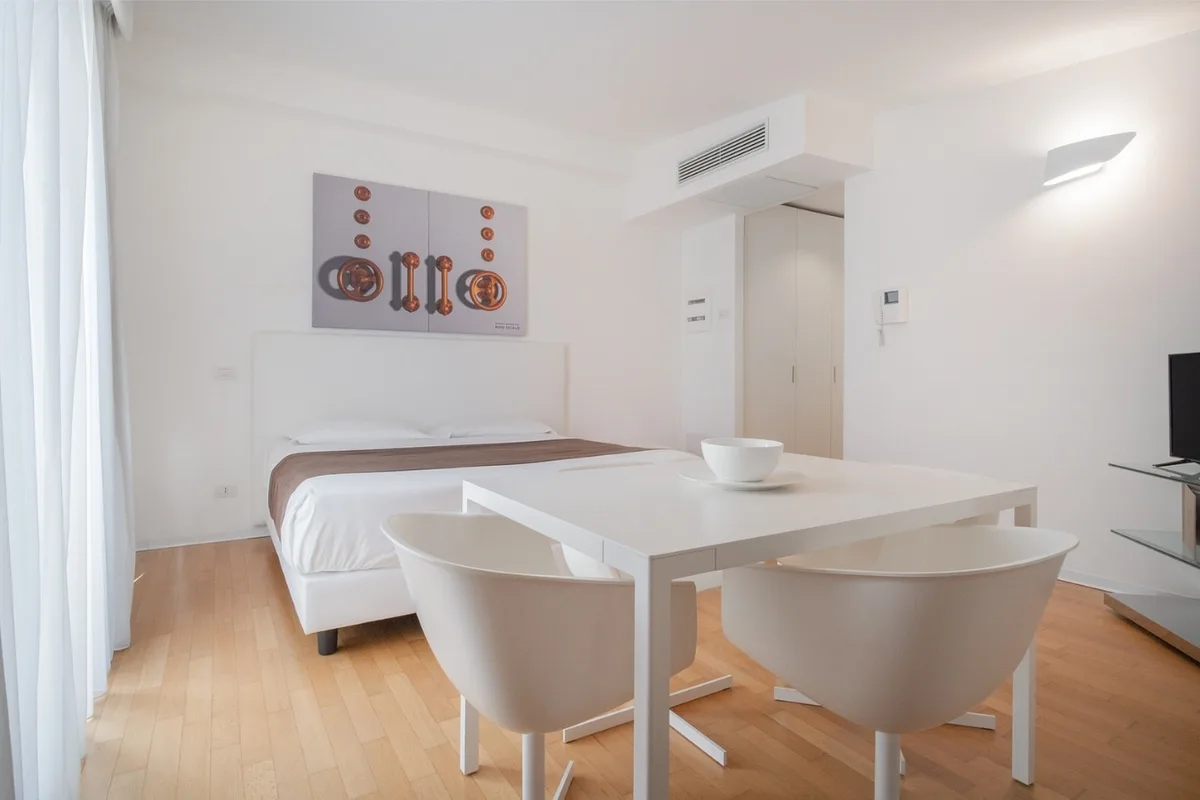 Studio con letto matrimoniale, tavolo bianco e sedie moderne