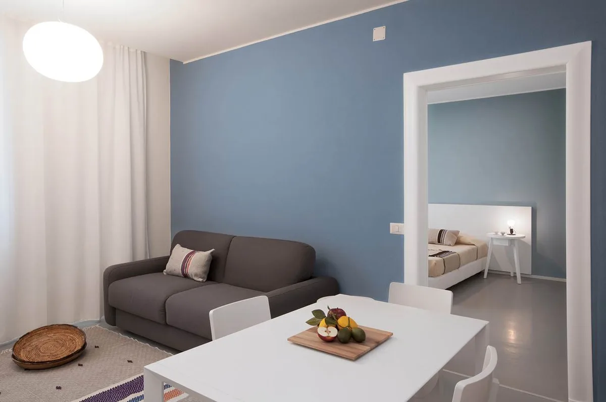 Soggiorno con divano grigio, parete azzurra e camera adiacente