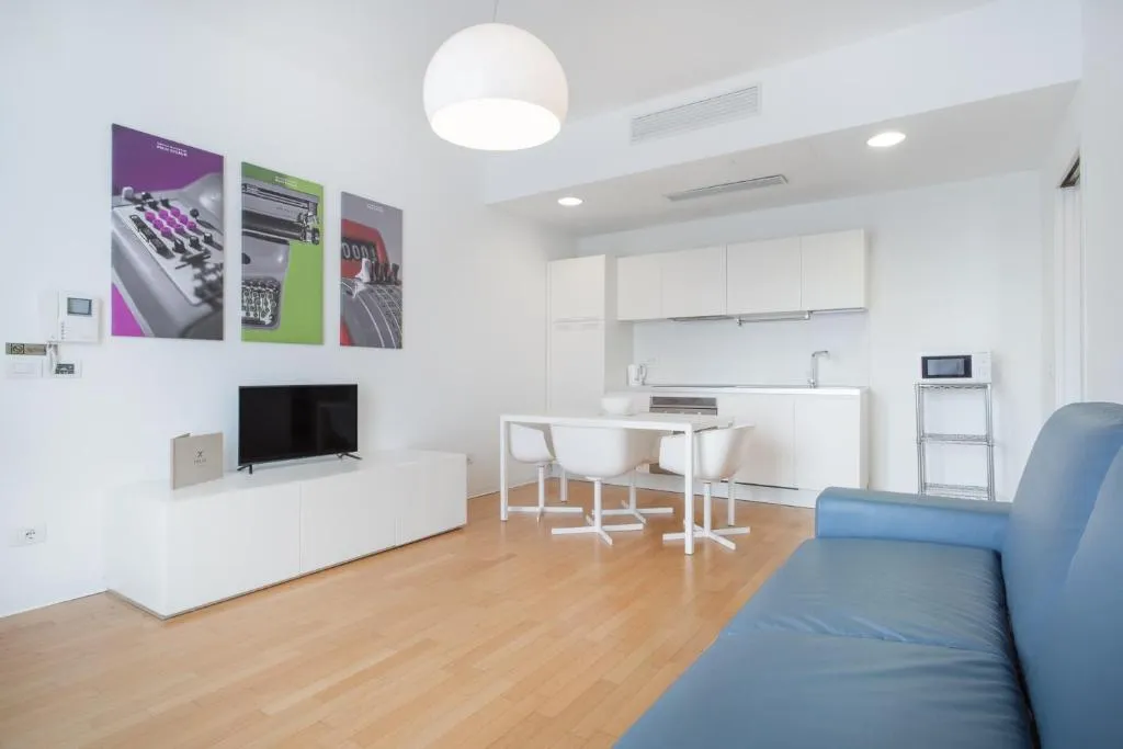 Salotto moderno con divano blu, TV, angolo cottura e quadri con macchine da scrivere vintage