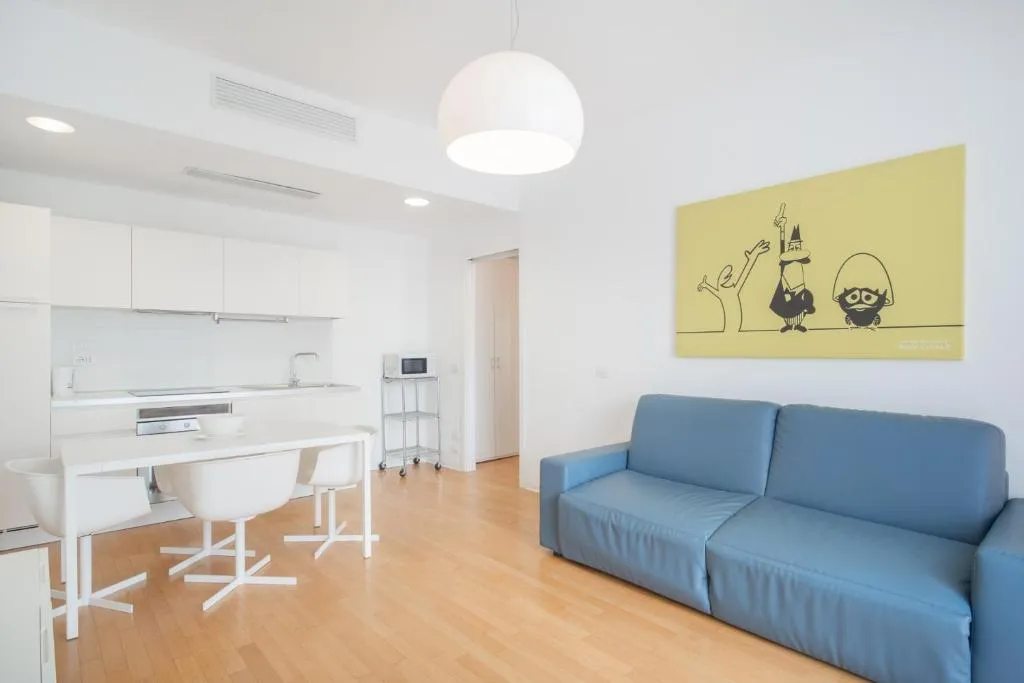 Soggiorno con divano blu, cucina bianca e tavolo da pranzo con quadro decorativo