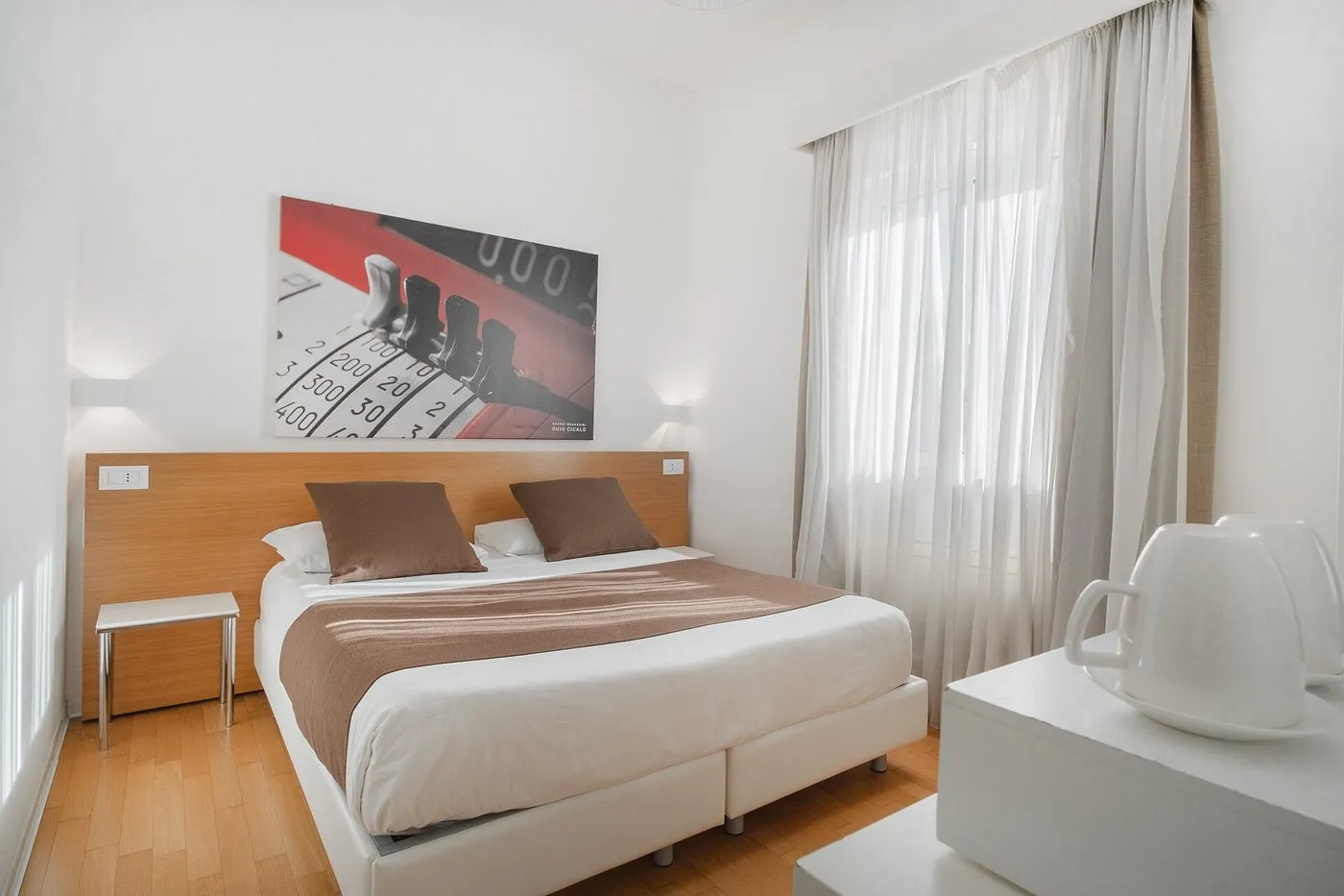 Camera matrimoniale con testiera in legno, biancheria bianca e marrone e quadro decorativo