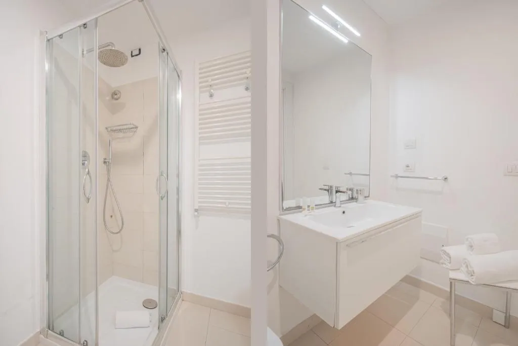 Bagno luminoso con doccia in vetro, lavabo bianco e ampio specchio
