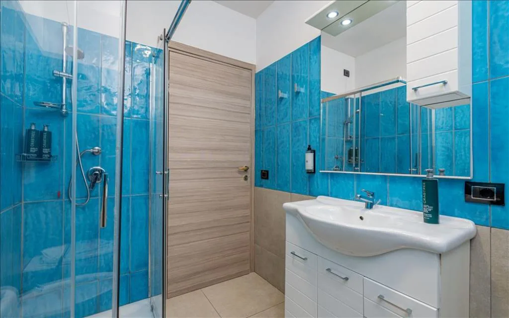Bagno con doccia, lavabo e piastrelle azzurre