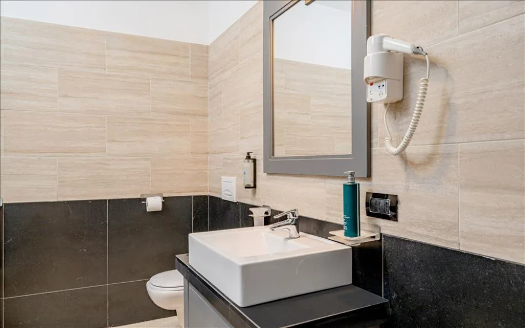 Bagno con lavabo, specchio, asciugacapelli e piastrelle beige e nere