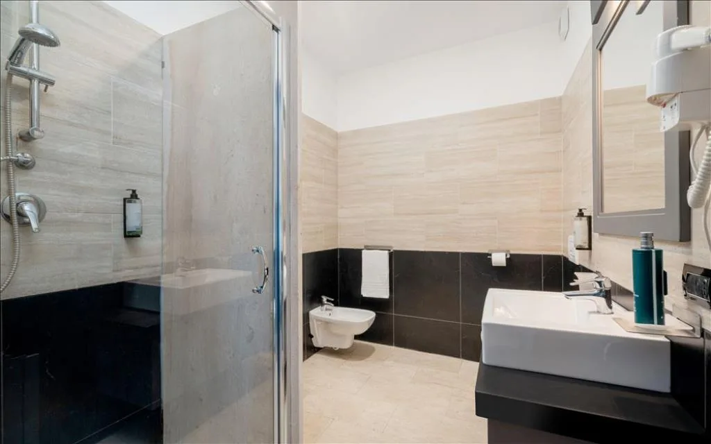 Bagno con doccia, lavabo squadrato, bidet e piastrelle beige e nere