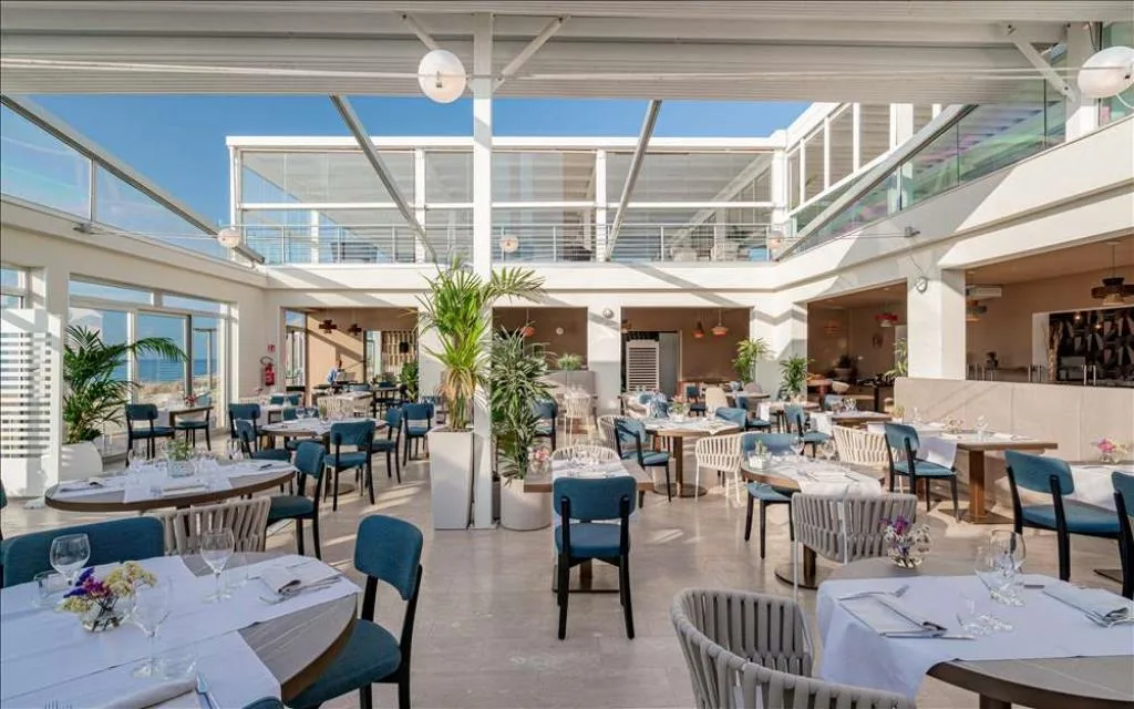 Sala ristorante con tavoli apparecchiati, piante e vetrate vista mare