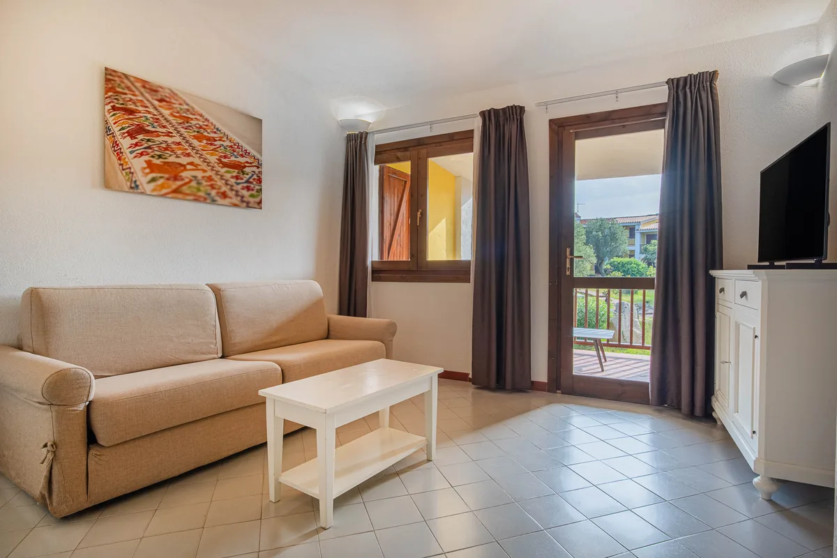 Soggiorno con divano beige, tavolino bianco e porta finestra sul giardino