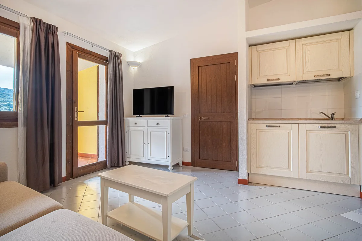 Soggiorno con angolo cottura, TV e accesso al balcone in appartamento del resort