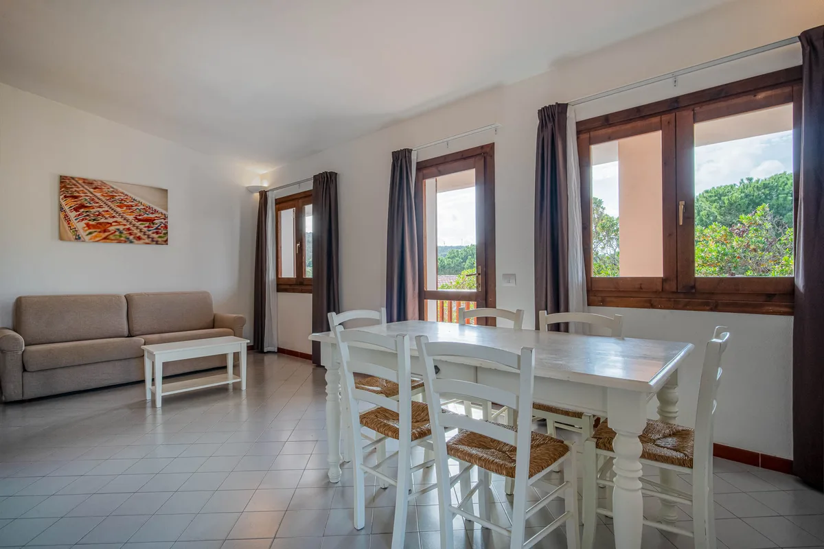 Zona pranzo con tavolo bianco, sedie impagliate e divano in appartamento luminoso