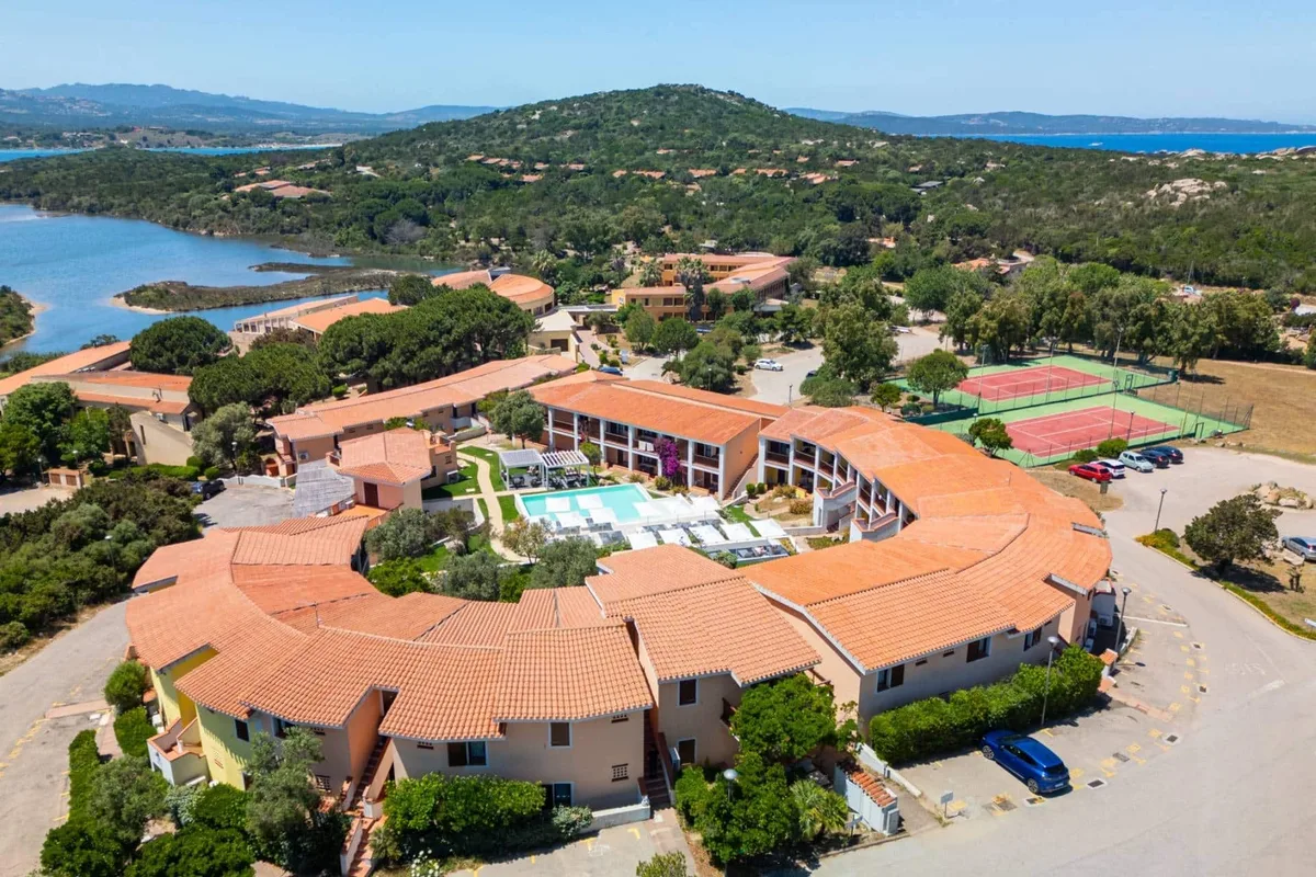 Veduta aerea del resort a semicerchio con piscina, campi da tennis e laguna