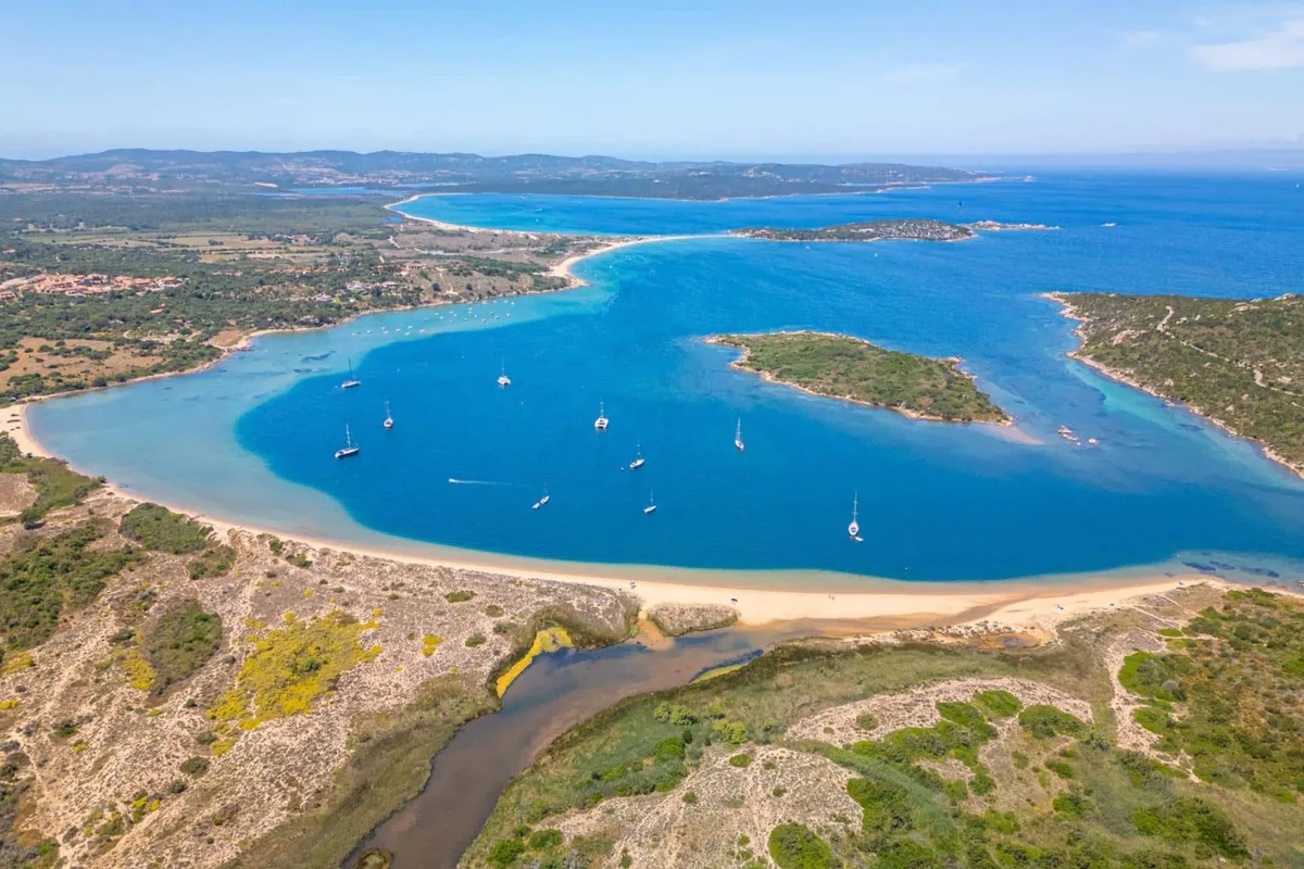 Panoramica aerea di laguna con barche a vela e lunga spiaggia sul mare blu