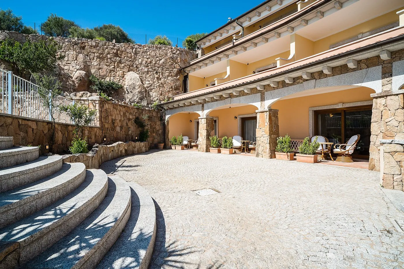 Cortile in pietra con portico ad archi, gradinata e poltrone in vimini