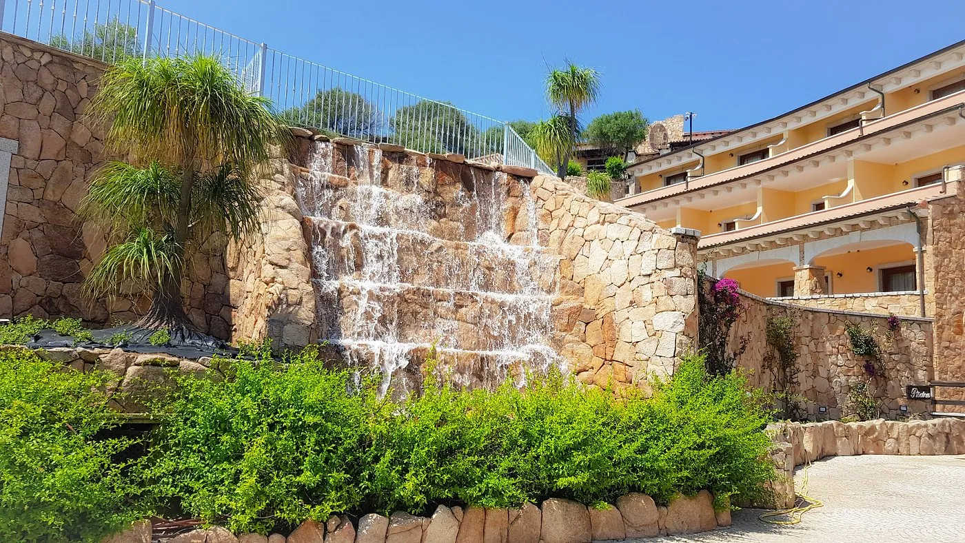 Cascata artificiale su parete in pietra con vegetazione e edificio giallo dell'hotel