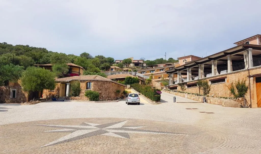 Piazzale in pietra con rosa dei venti e edifici dell'hotel circondati da colline verdi