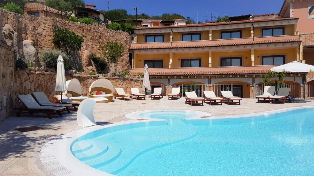 Piscina con lettini e ombrelloni davanti all'edificio giallo dell'hotel