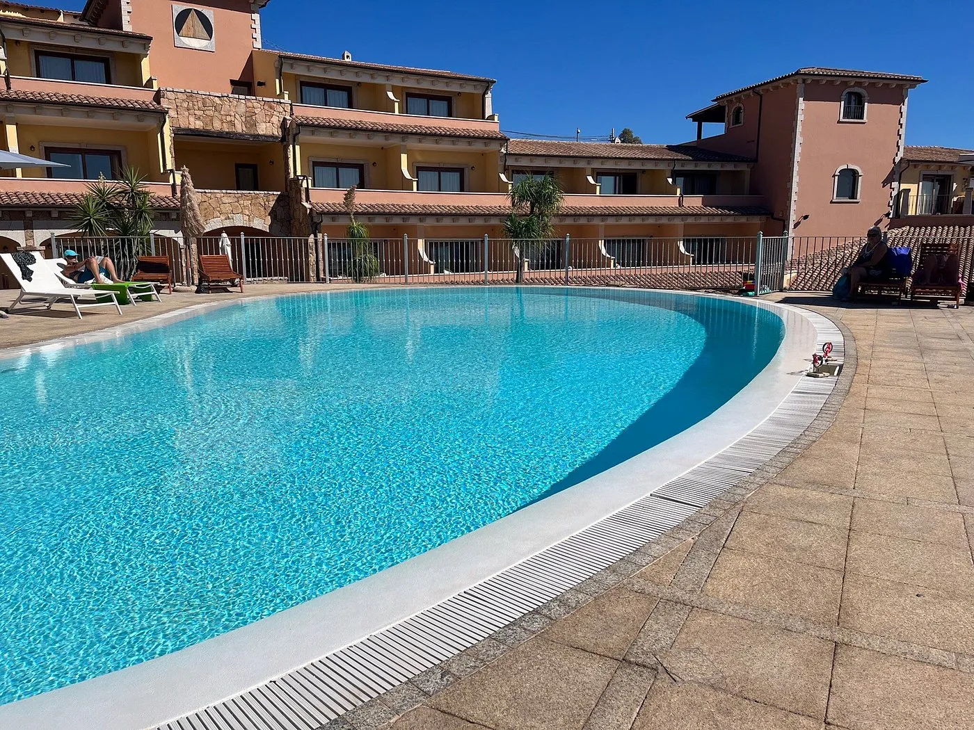 Ampia piscina dell'hotel con ospiti e edificio in pietra rosa sullo sfondo