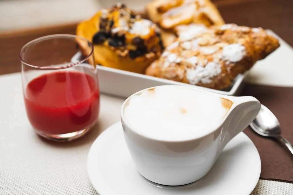 Colazione con cappuccino, succo rosso e cornetti dolci
