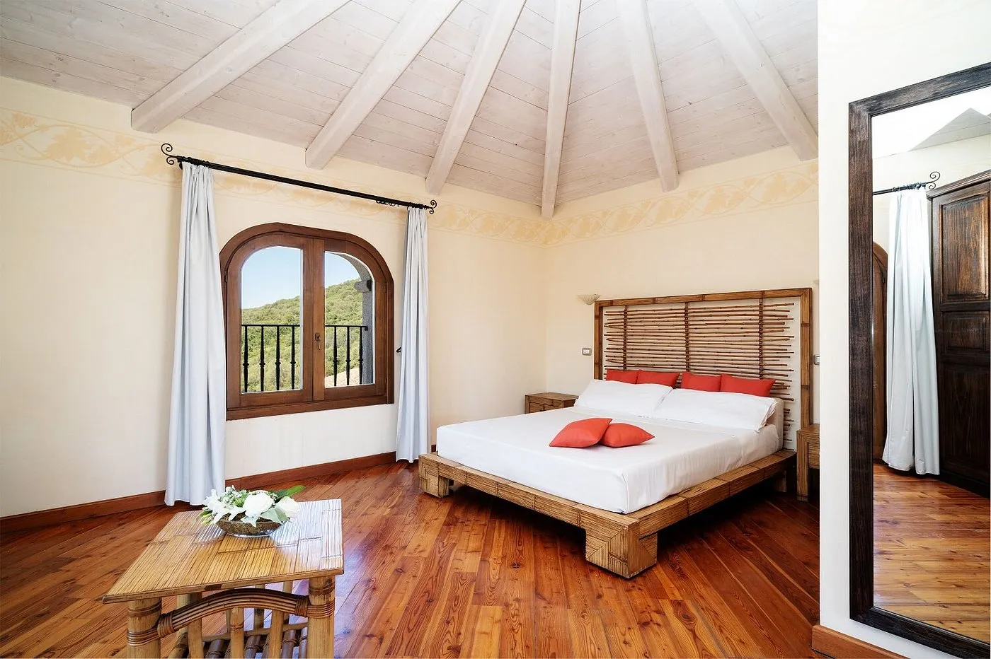 Camera con letto in bambù, pavimento in legno, soffitto a travi e finestra ad arco