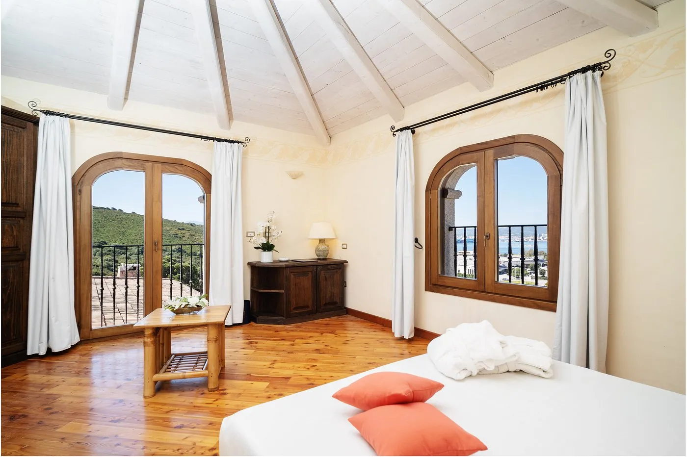 Camera luminosa con letto, soffitto in legno e finestre ad arco con vista sul mare