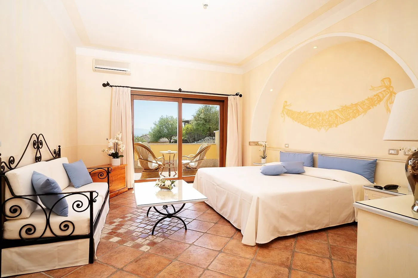 Camera con letto matrimoniale, divano con cuscini azzurri e uscita sul balcone