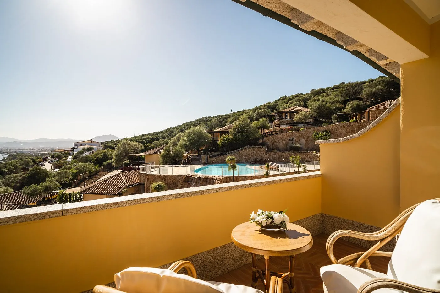 Balcone della camera con poltrone in vimini e vista sulla piscina e le colline