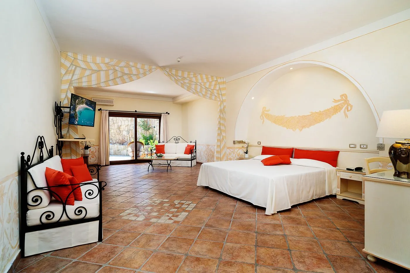 Suite ampia con letto, area soggiorno con divani e cuscini rossi