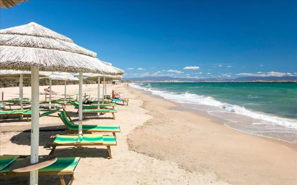 Spiaggia di sabbia con ombrelloni in paglia e lettini verdi affacciati sul mare turchese