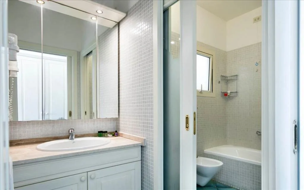 Bagno con lavabo, ampio specchio e vasca con piastrelle a mosaico chiare