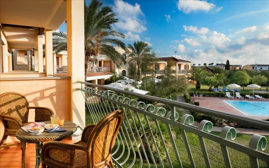 Balcone con tavolino e sedie in vimini affacciato sul giardino e la piscina dell'hotel