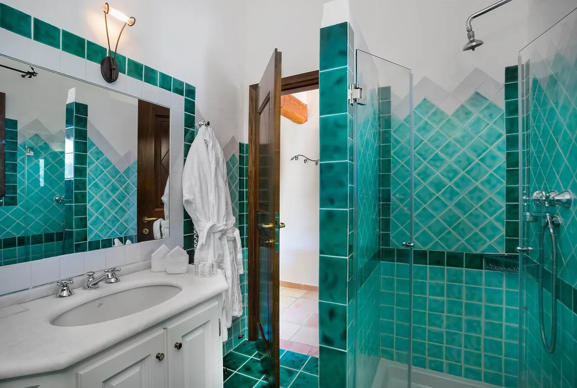 Bagno con piastrelle verdi, doccia in vetro e lavabo in marmo con accappatoio