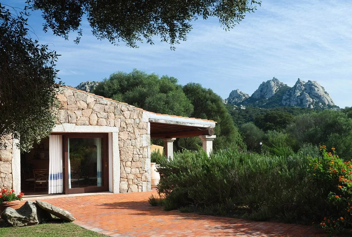 Casa in pietra con pergolato e vista sulle montagne rocciose immersa nel verde
