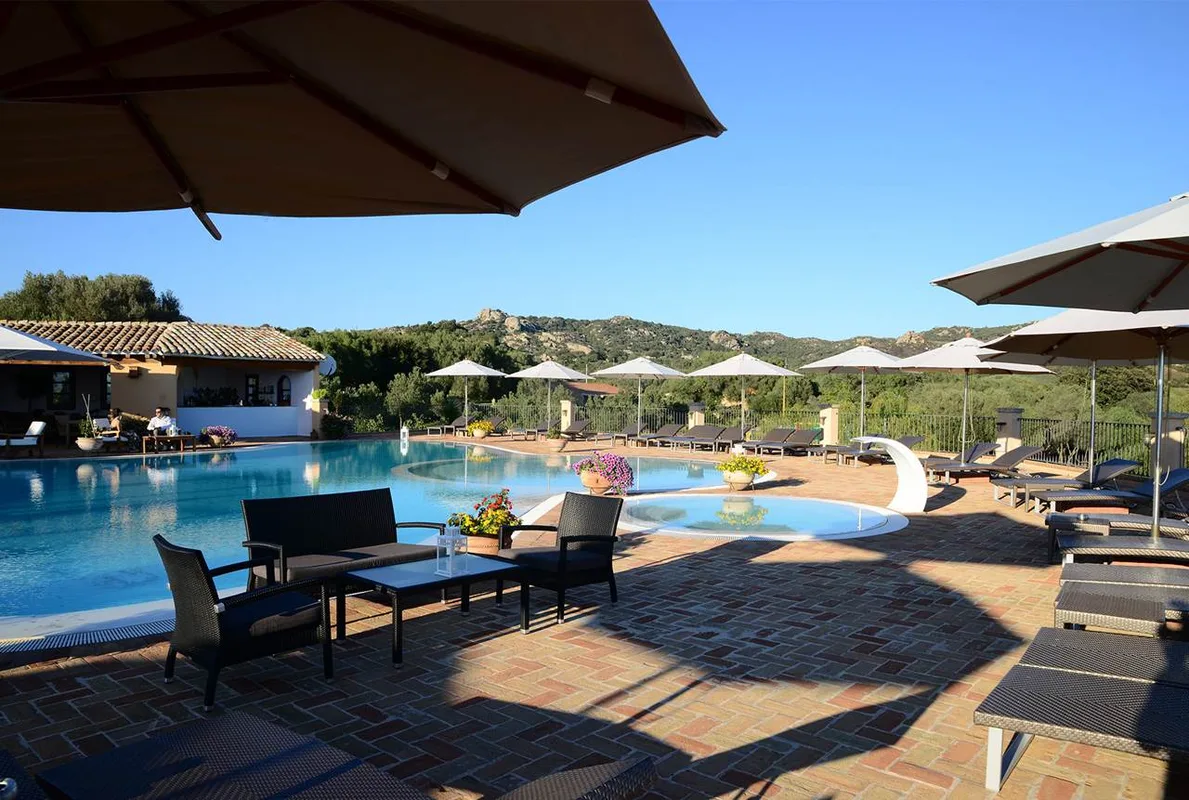 Area piscina con lettini, ombrelloni e zona relax in cotto immersa nel verde