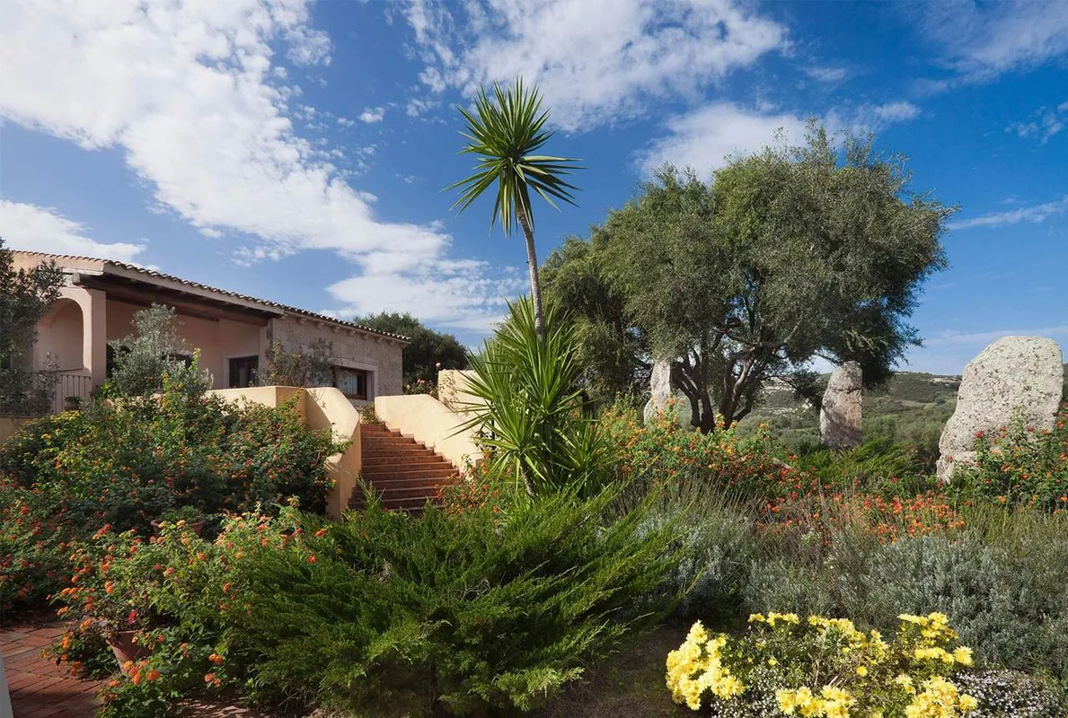 Giardino fiorito con scalinata, palma e ulivi davanti a una villetta