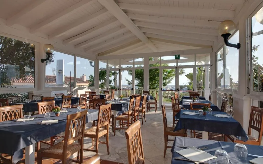 Sala ristorante con tovaglie blu, soffitto in legno bianco e vista mare