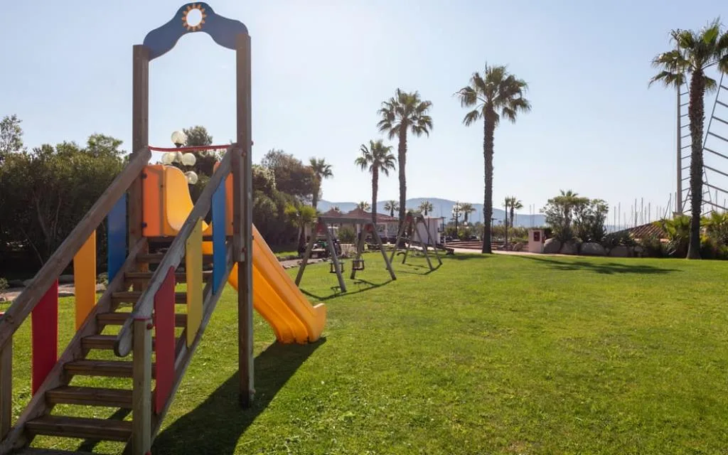 Parco giochi per bambini con scivolo colorato e altalene su prato verde