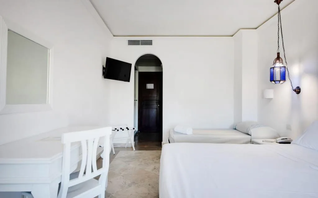 Camera bianca essenziale con letti, scrivania e lampada in vetro blu