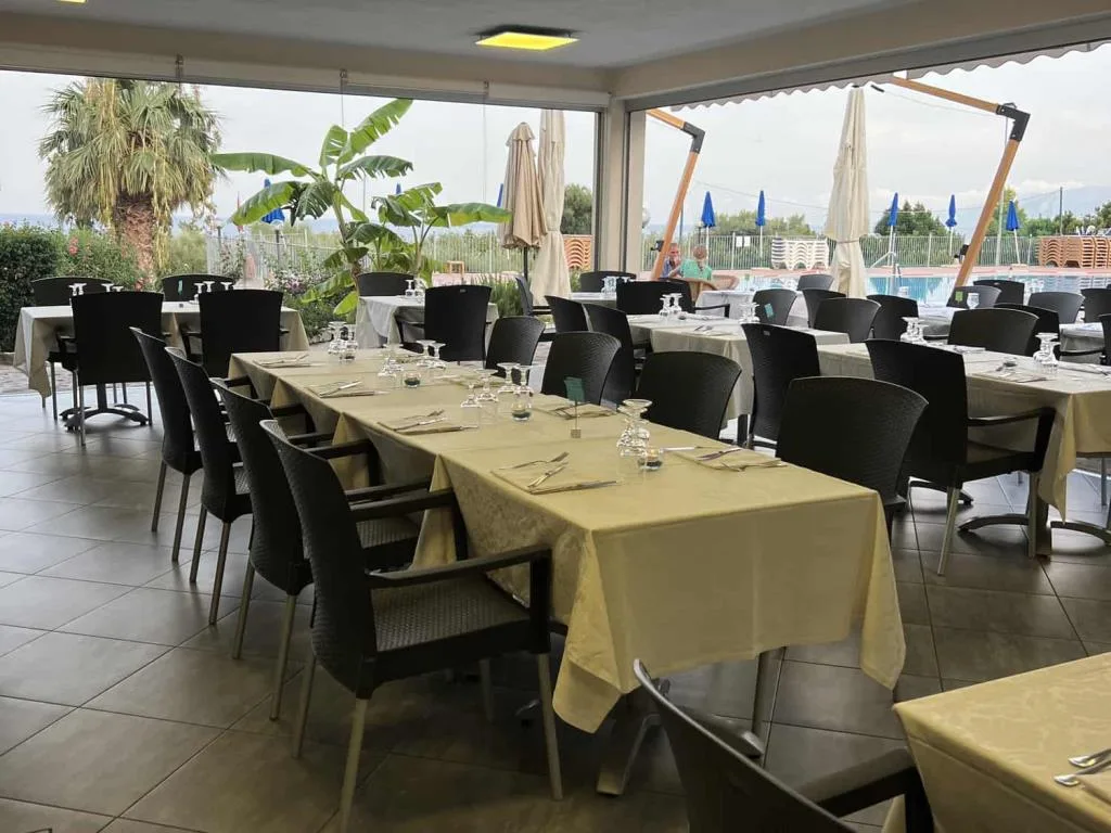 Sala ristorante luminosa con tavoli apparecchiati e vista sulla piscina e il verde