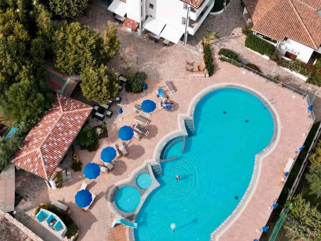 Vista aerea della piscina con ombrelloni blu e lettini circondata dagli edifici dell'hotel