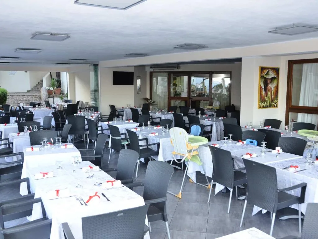 Sala ristorante con tavoli apparecchiati con tovaglie bianche e seggioloni per bambini