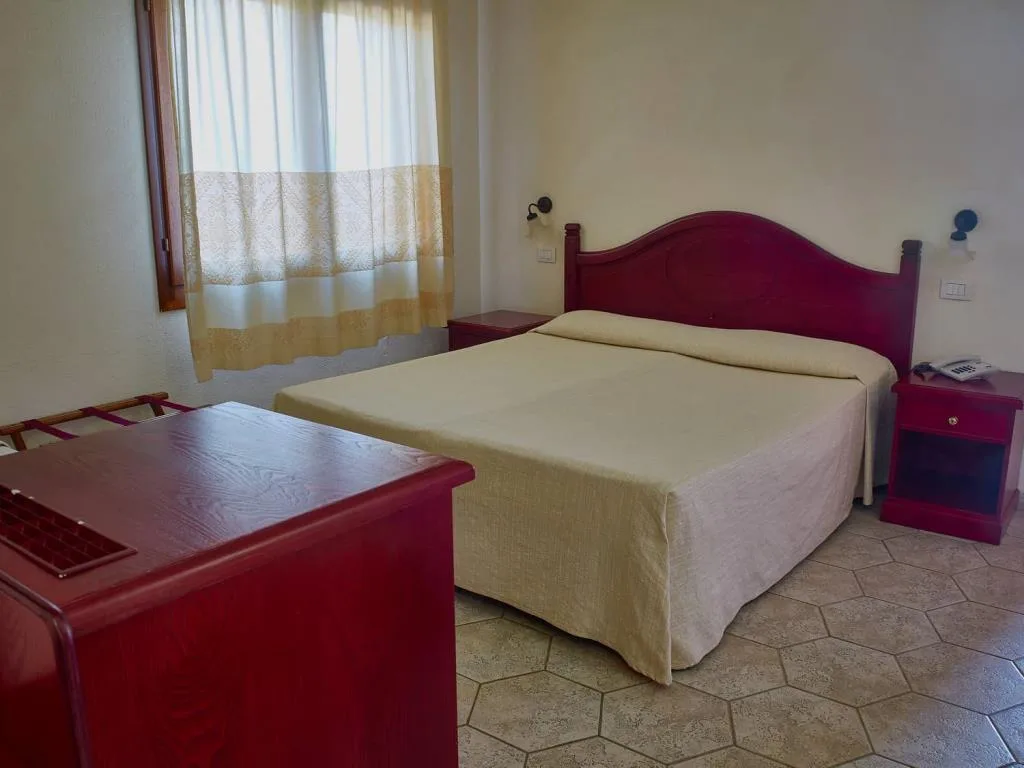 Camera con letto matrimoniale, testiera in legno rosso e finestra con tende
