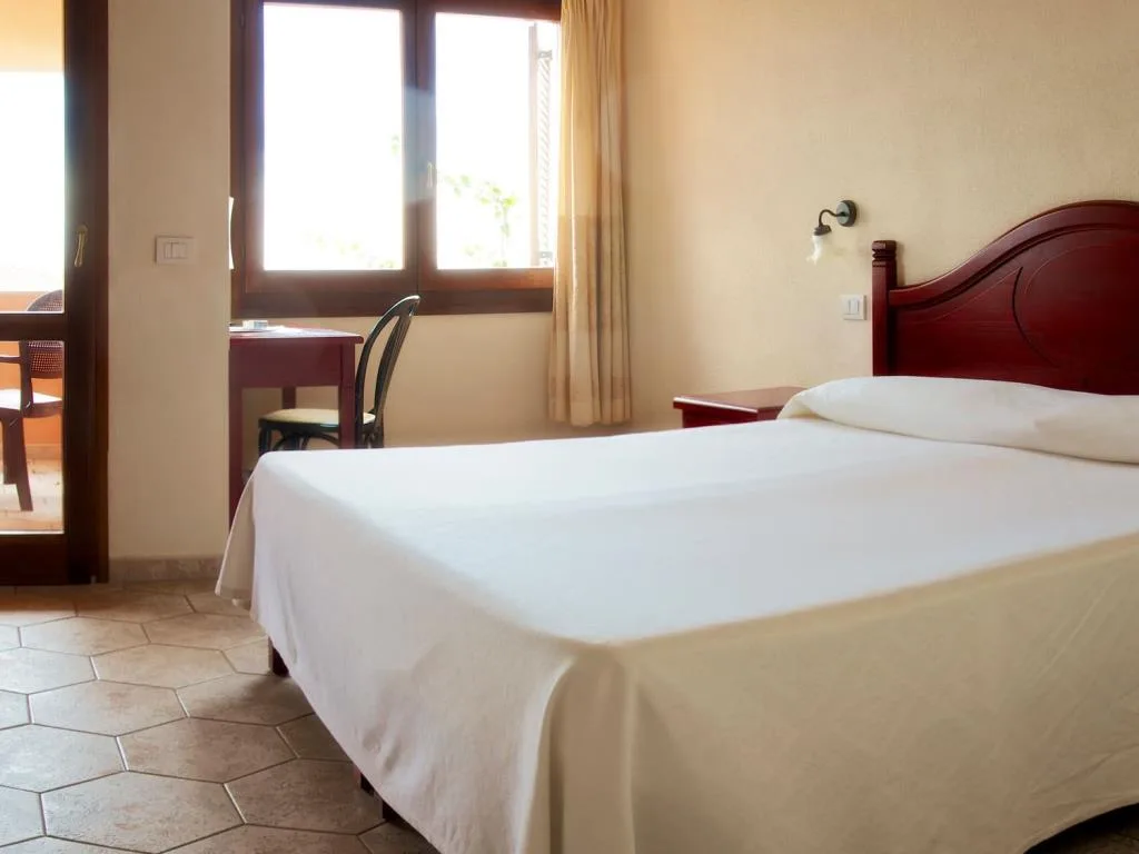 Camera con letto matrimoniale, scrivania e accesso al balcone con tende chiare