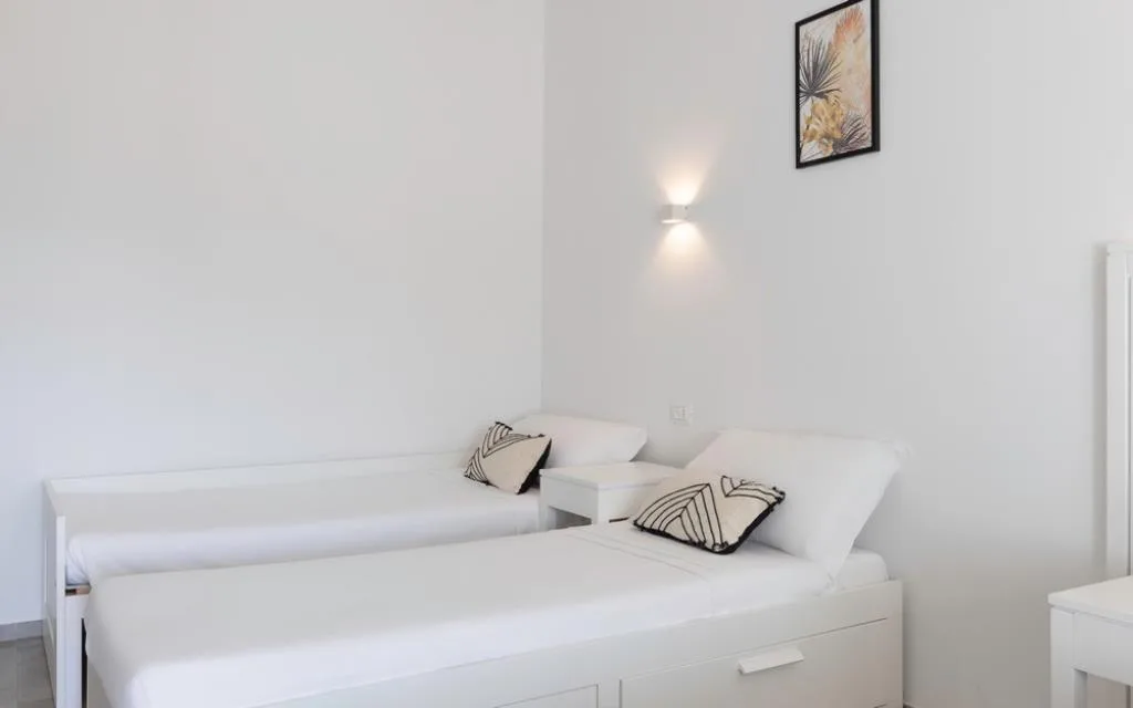Dettaglio camera con letti singoli bianchi e cuscini decorativi