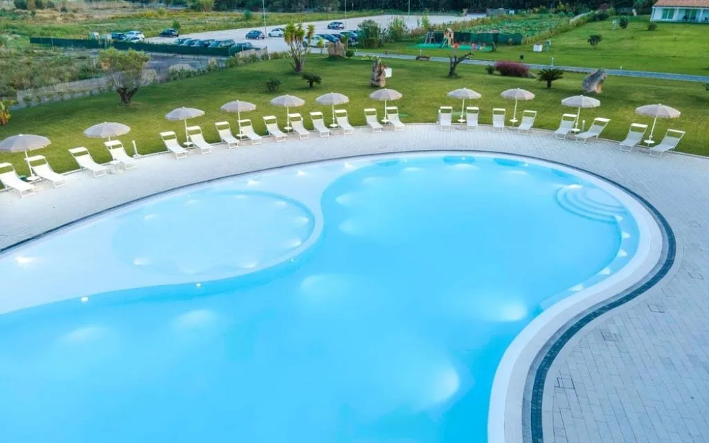 Veduta aerea della piscina curva con lettini e ombrelloni nel giardino