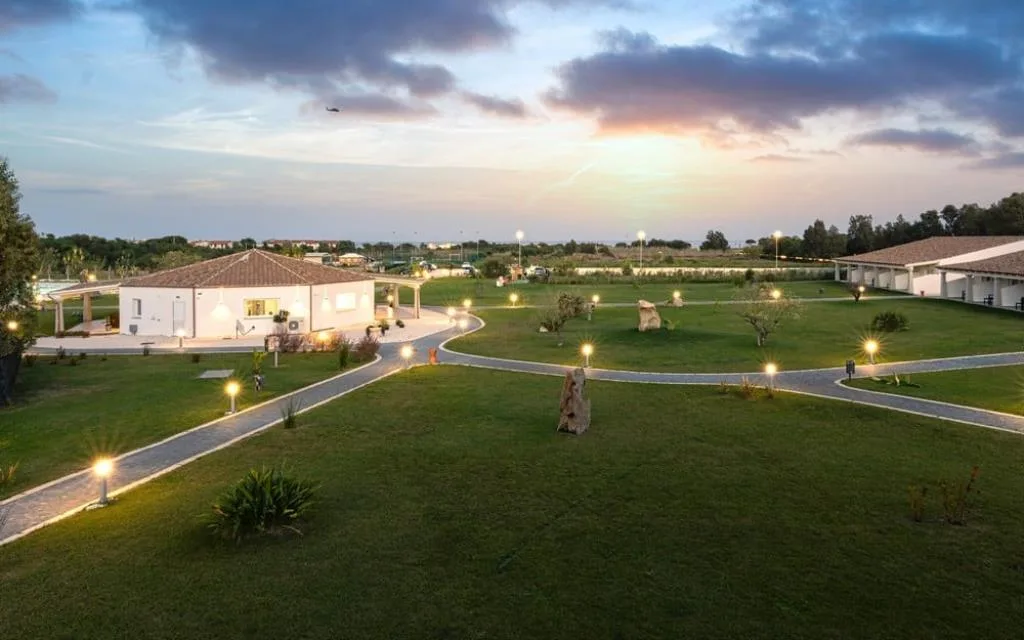 Veduta panoramica del resort con giardini e vialetti illuminati al tramonto