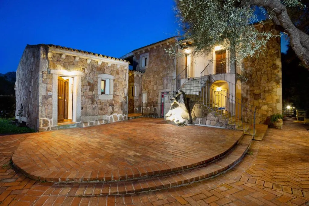 Edificio in pietra illuminato di sera con cortile in cotto e scala