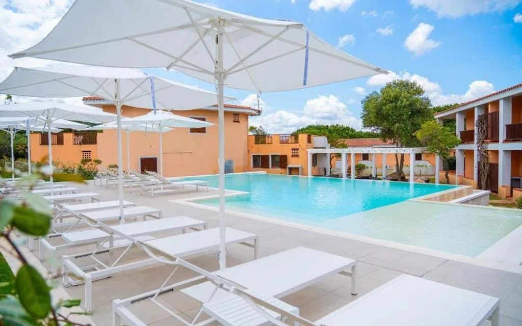 Piscina con lettini bianchi e ombrelloni circondata dagli edifici
