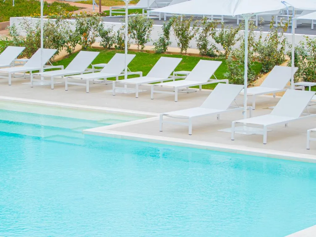Dettaglio della piscina con lettini bianchi allineati e ombrellone vicino al giardino