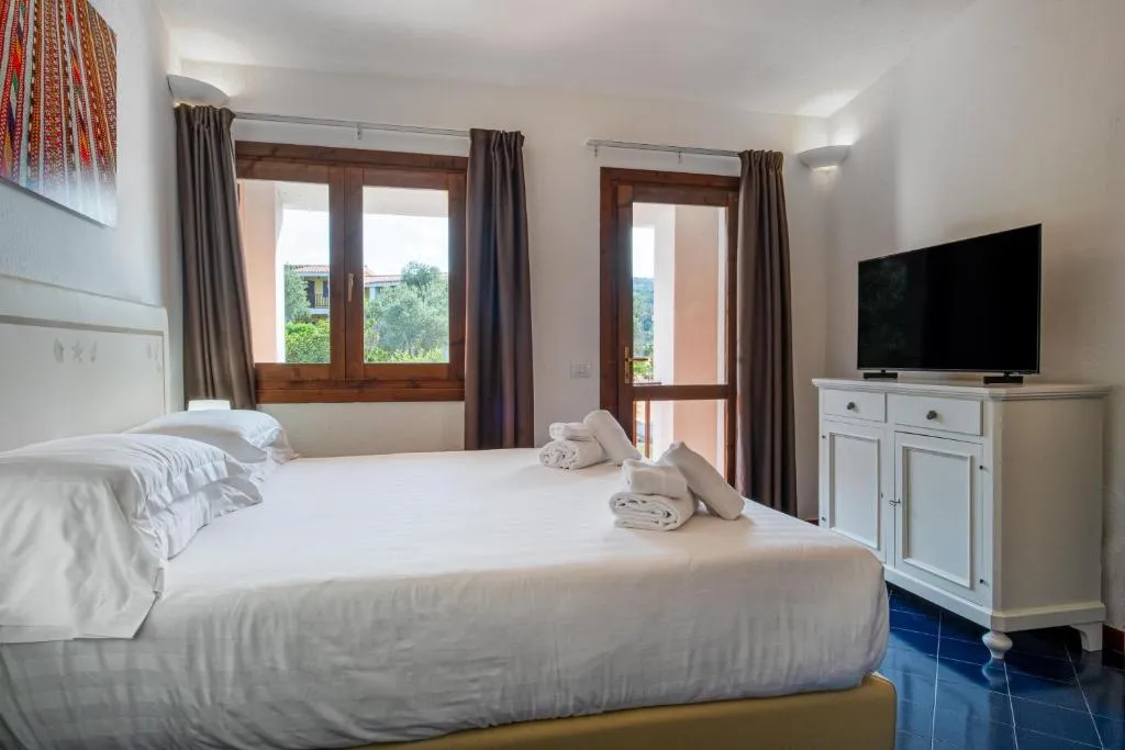 Camera matrimoniale luminosa con letto bianco, TV a parete, comò e ampie finestre
